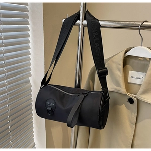 Detailed close-up of a black cylinder crossbody bag with adjustable wide fabric strap