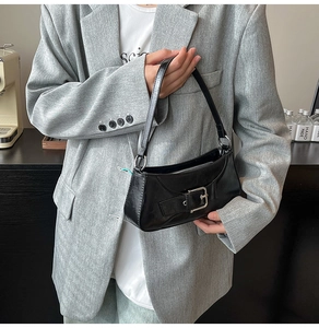 Detail view of the black underarm bag with silver buckle worn by a model in a gray blazer