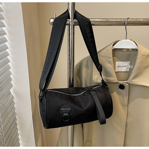 Detail of black nylon barrel bag featuring wide branded strap and round logo patch