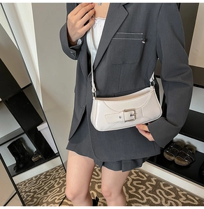 Detail of a creamy white underarm bag with metal buckle on a grey suit outfit