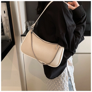 Close-up of cream shoulder bag featuring textured finish and decorative metal chain