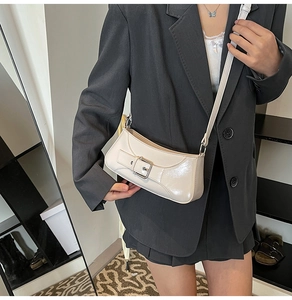 Detail of a creamy white half-moon underarm bag in glossy patent leather with silver buckle