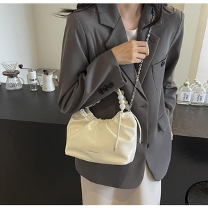 Detail of cream pleated crossbody bag with pearl handle and silver chain on model