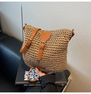 Detailed straw woven texture of a cross-body beach bag with brown leather strap and buckle