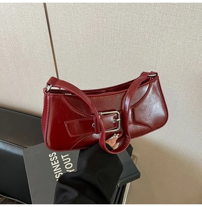 Detail of dark red baguette bag with glossy cracked leather texture and metal buckle