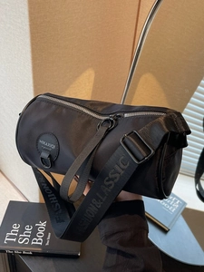 Fashionable black cylindrical crossbody bag with wide logo strap and nylon finish