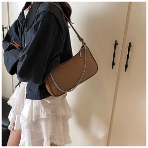 Detail of a brown woven shoulder bag with silver chain strap worn with a navy outfit