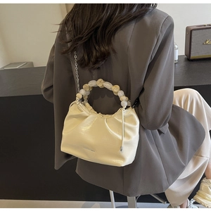 Detail of a pleated cream dumpling bag with beaded handle and silver chain strap