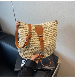 Detail of hand-woven straw shoulder bag with brown leather strap and gold hardware