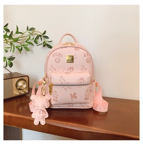Close-up of pink litchi grain leather backpack with bear charm on a wooden table