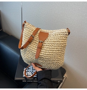 Close-up of beige woven straw bag with adjustable brown leather strap and buckle detail