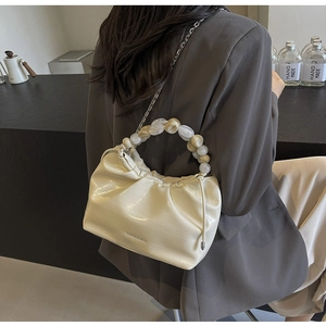 Detail of off-white pleated dumpling bag featuring agate-style beaded handle and silver chain