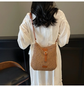 Close-up of a brown woven straw crossbody bag with leather strap and metal buckle detail