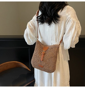 Detail of woven straw shoulder bag featuring brown leather strap and buckle closure