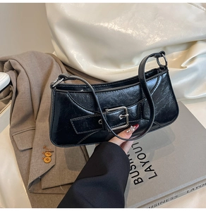 Detailed close-up of shiny black patent leather shoulder bag with silver metal buckle