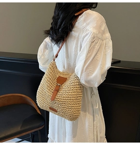 Detail of a beige woven straw crossbody bag featuring a brown leather strap and buckle