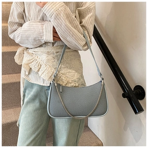 Light blue woven underarm bag with silver chain strap shown on model in a natural setting