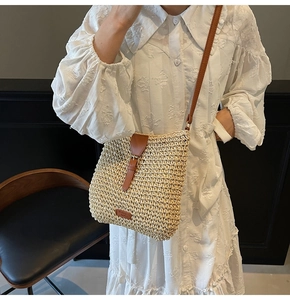 Close-up of beige woven straw crossbody bag with brown leather strap and brand patch