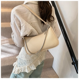 Close-up of beige woven crescent bag featuring silver chain detail and leather strap