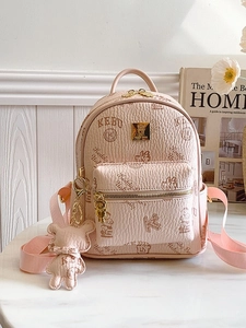 Pink mini faux leather backpack with bear prints and matching bear charm on a marble table