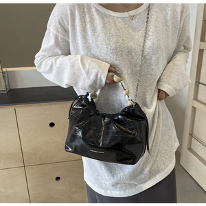 Detail of black pleated bag with pearl handle and metal chain in lifestyle setting