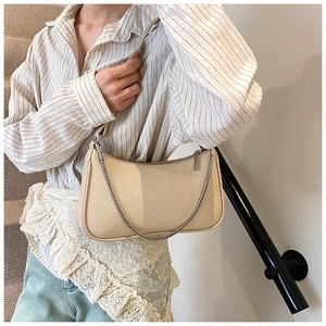 Close-up of beige woven baguette bag featuring a gold chain and leather strap detail
