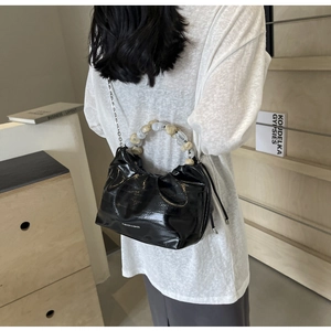 Detail of black pleated dumpling bag featuring marble bead handle and silver chain strap