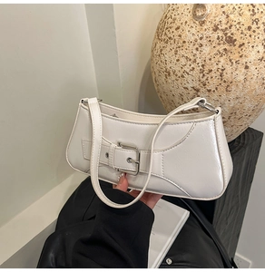 Detail shot of the white patent leather shoulder bag with a bold buckle strap and zipper