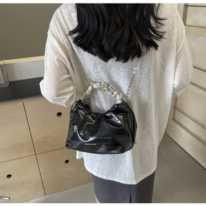 Detail of black glossy pleated dumpling bag with large bead handle and metal chain strap