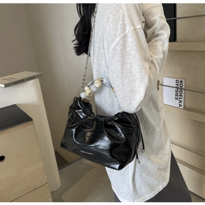 Detail of glossy black dumpling bag featuring marble bead handle and silver chain strap