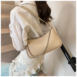 Detail view of beige woven underarm bag with silver chain strap on a model