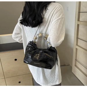 Detail of black pleated crossbody bag featuring oversized textured bead handle and silver chain