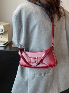 Minimalist deep red leather baguette underarm bag with silver buckle worn on a grey blazer