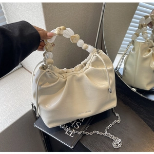 Detail of beige pleated bag with crocodile pattern and amber bead handle shown in mirror