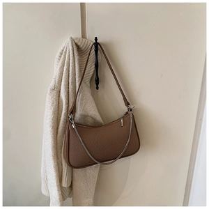 Brown woven baguette bag with silver chain detail hung against a white wall background