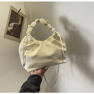 Detail of cream pleated dumpling bag with elegant beaded handle and gold chain strap