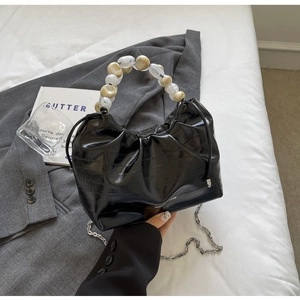 Detail of glossy black pleated dumpling bag featuring artistic beaded handle and chain