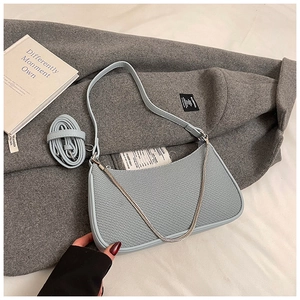 Detail of light blue shoulder bag with metal chain on textured gray fabric background