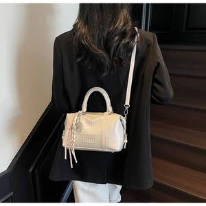 Detalle de bolso Boston crema con relieve HDB y adorno de borla llevado por una modelo