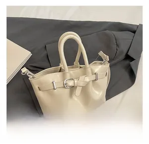 Detail shot of a cream-colored bucket bag with glossy finish and metal belt buckle