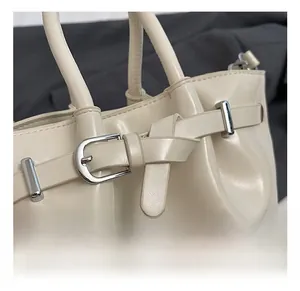 Detail of beige bucket bag featuring shiny faux leather and silver metal buckle
