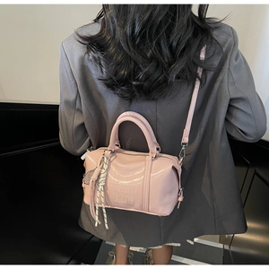 Detalle de bolso bowling de piel suave rosa con relieve de letras y correa de hombro ajustable
