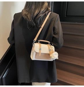 Detail shot of elegant cream and brown crossbody bag with decorative fur ball on side