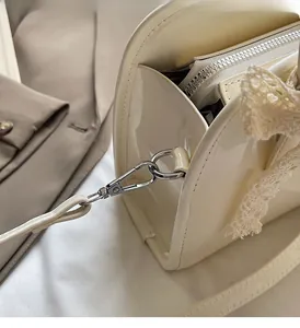Detail of glossy cream leather shoulder bag with silver hardware and lace bow
