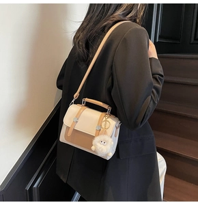 Detail view of two-tone crossbody bag featuring a plush charm and adjustable shoulder strap