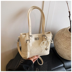 Close-up of beige quilted bucket bag with pearl bow charm and silver hardware details