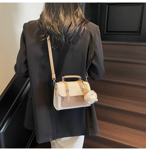 Detail of color-block shoulder bag featuring white and camel leather with a plush charm