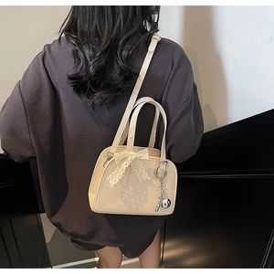 Detail of beige patent leather Boston bag with lace bow and silver metal charm