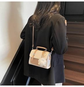 Detail of two-tone beige and brown handbag with a cute plush charm and long strap