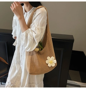 Détail du sac cabas en tricot marron avec fleur blanche porté à l'épaule par le mannequin